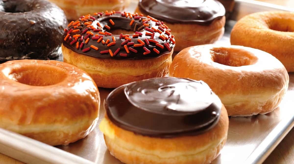 Assortment of ring doughnuts, including chocolate frosted with sprinkles, plain glazed, and chocolate glazed.
