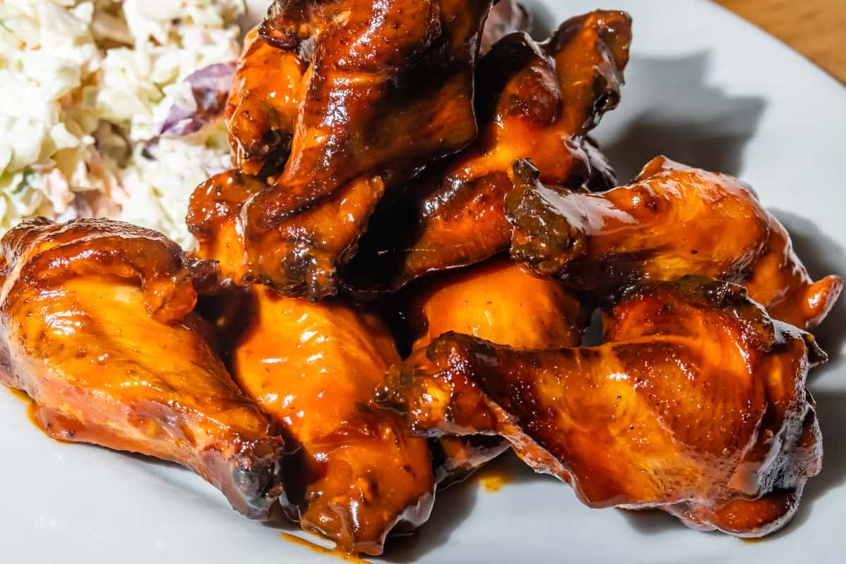 Close-up of saucy barbecue chicken wings glazed in a rich, smoky sauce, served with a side of creamy coleslaw. A bold, flavor-packed appetizer or entrée, perfect for fans of classic American grill fare.