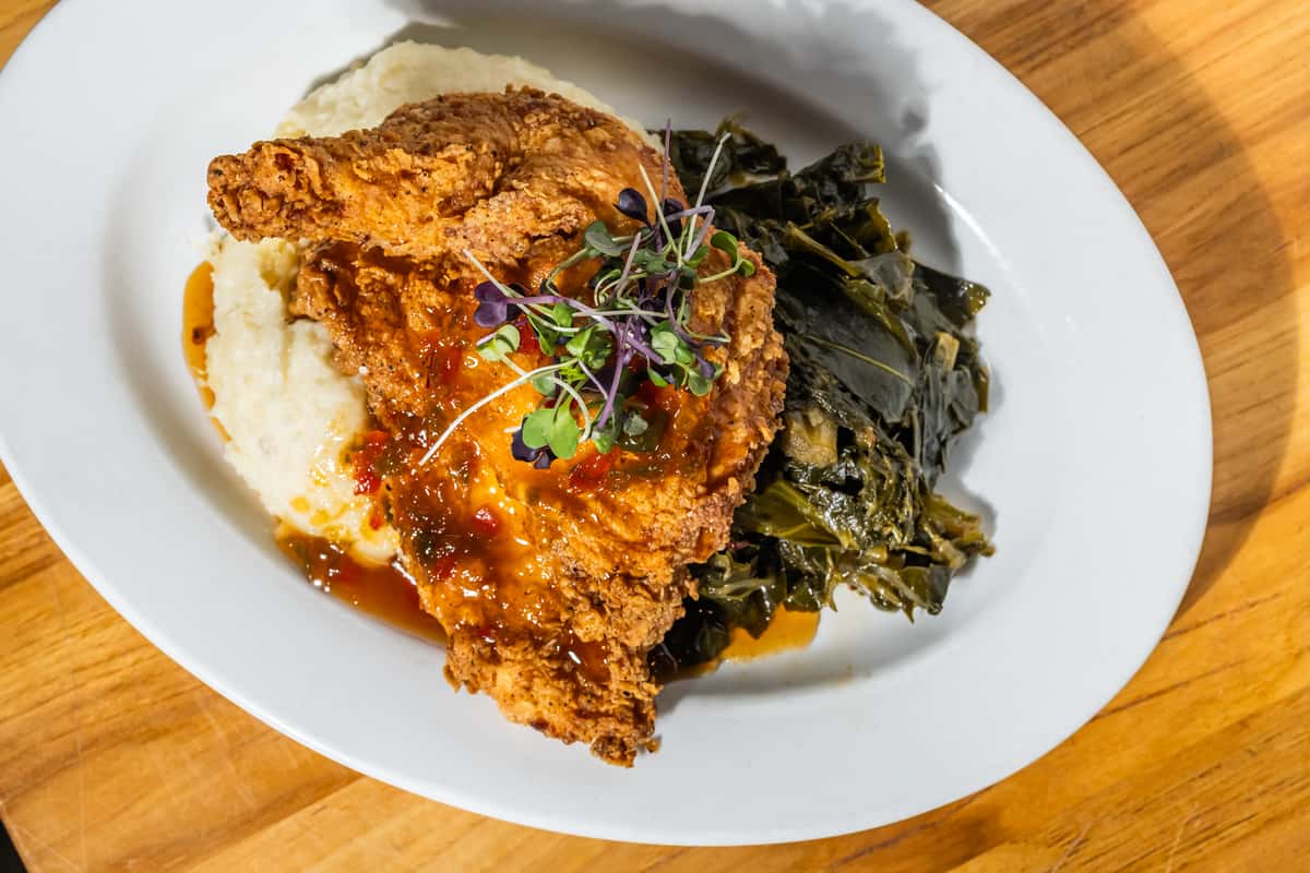 Crispy fried chicken breast glazed with a sweet and spicy sauce, served over creamy mashed potatoes and braised collard greens, garnished with microgreens. A soulful Southern dish with a modern presentation.