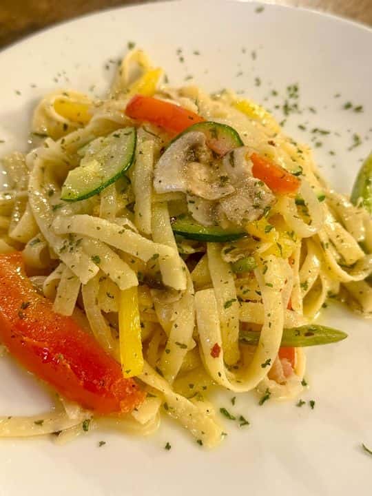Vegetable fettuccine pasta tossed with sautéed zucchini, mushrooms, and bell peppers in a light garlic herb sauce, plated at an Italian-inspired restaurant.