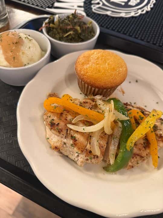 Grilled chicken breast topped with sautéed bell peppers and onions, served with mashed potatoes, collard greens, and a cornbread muffin for a Southern-style plate lunch.