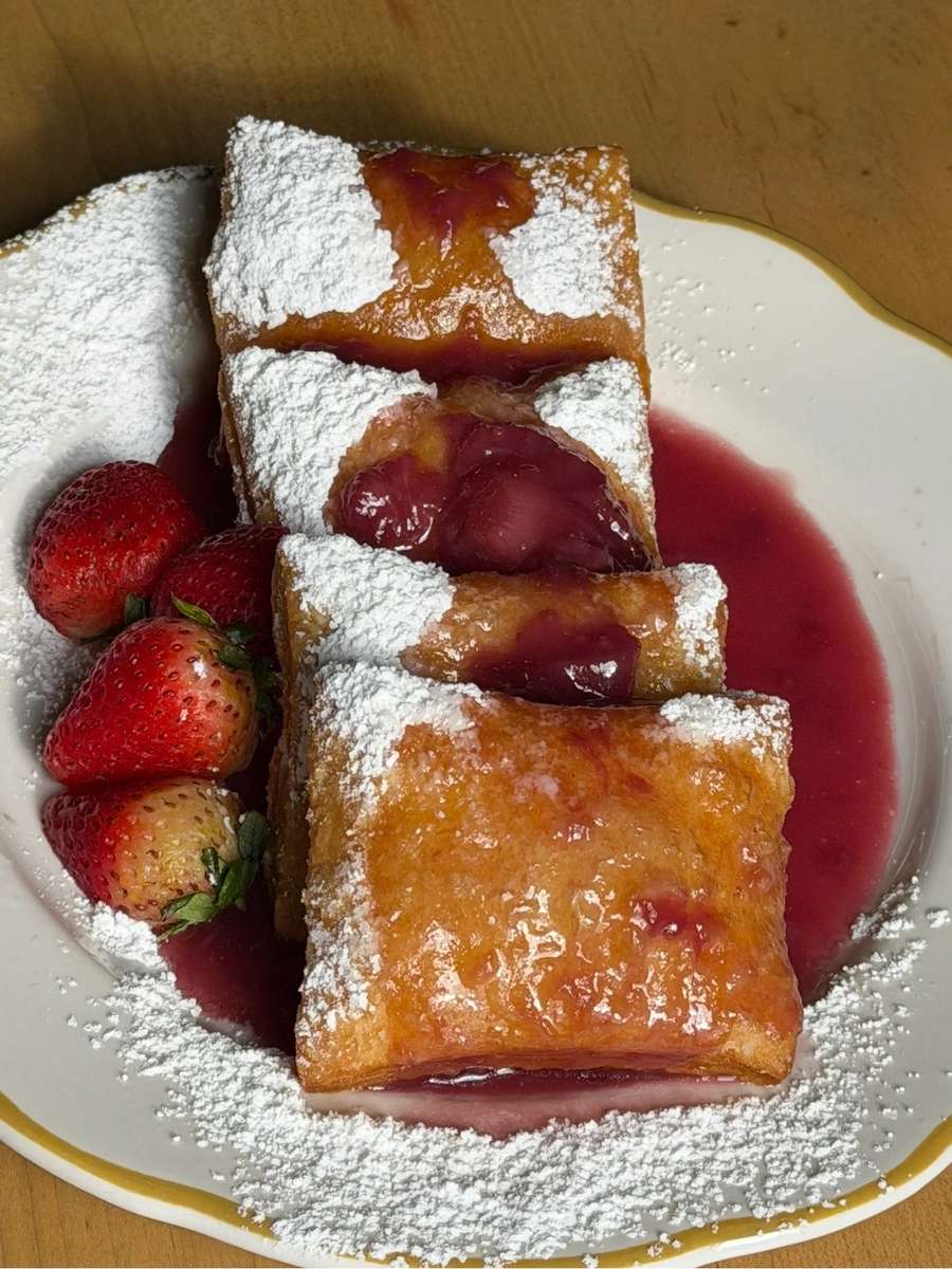 Golden, flaky strawberry cream cheese pastries dusted with powdered sugar, served with fresh strawberries and sweet strawberry sauce on a white dessert plate.