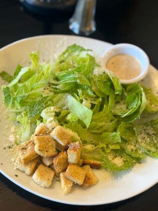 Classic Caesar salad with crisp romaine lettuce, garlic croutons, grated Parmesan, and creamy dressing served on a white plate.