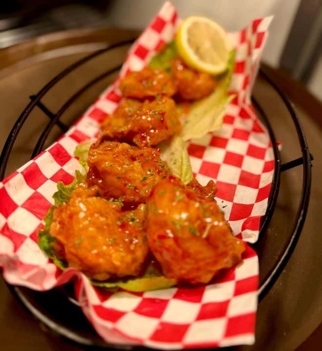 Crispy fried shrimp bites tossed in sweet and spicy sauce, served in a red checkered basket with lettuce and a fresh lemon wedge at a Southern seafood restaurant.