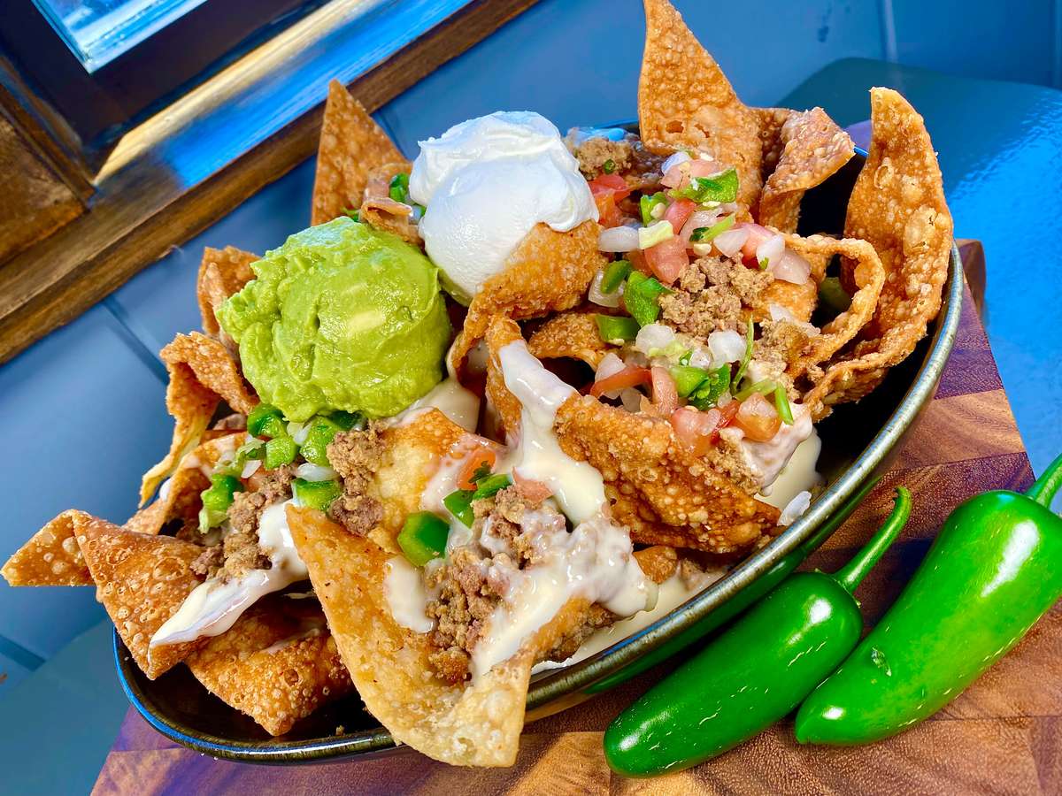Loaded nachos with guacamole and toppings, with whole jalapeños on the side