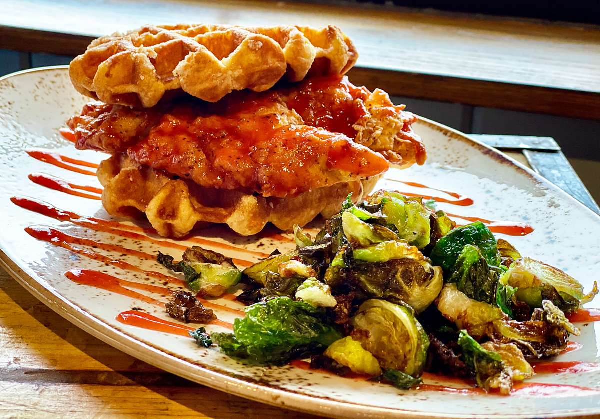 Chicken and waffles topped with sauce, served with Brussels sprouts on the side