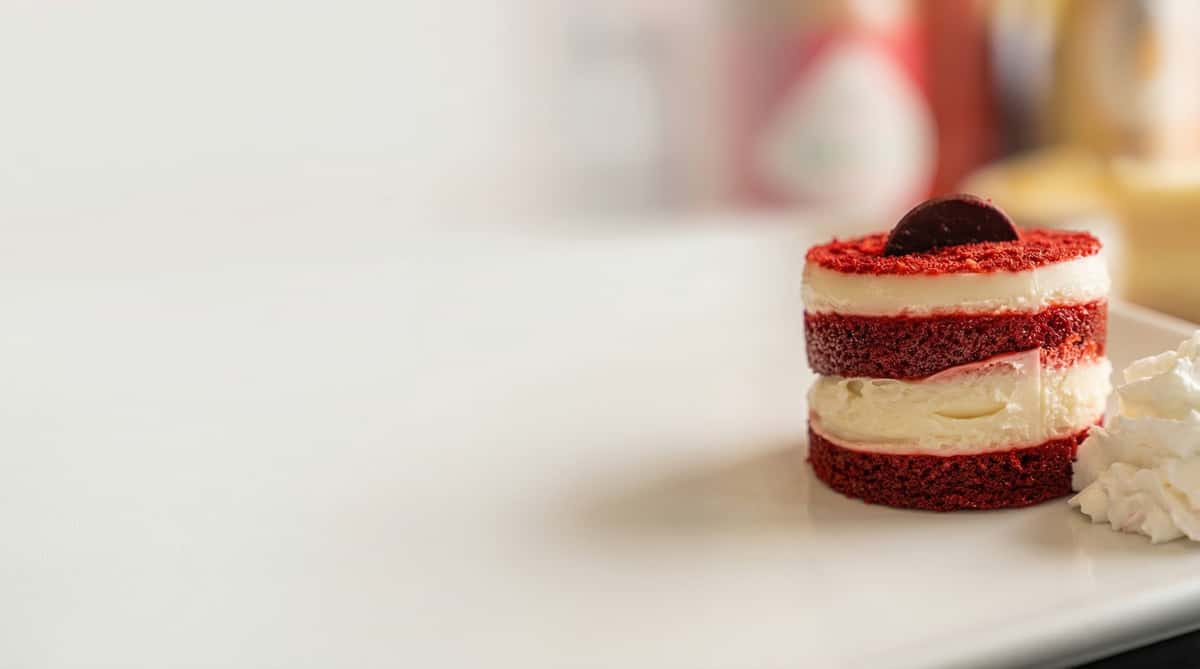 Layered red velvet dessert with cream filling and whipped topping served on a white plate at a restaurant.