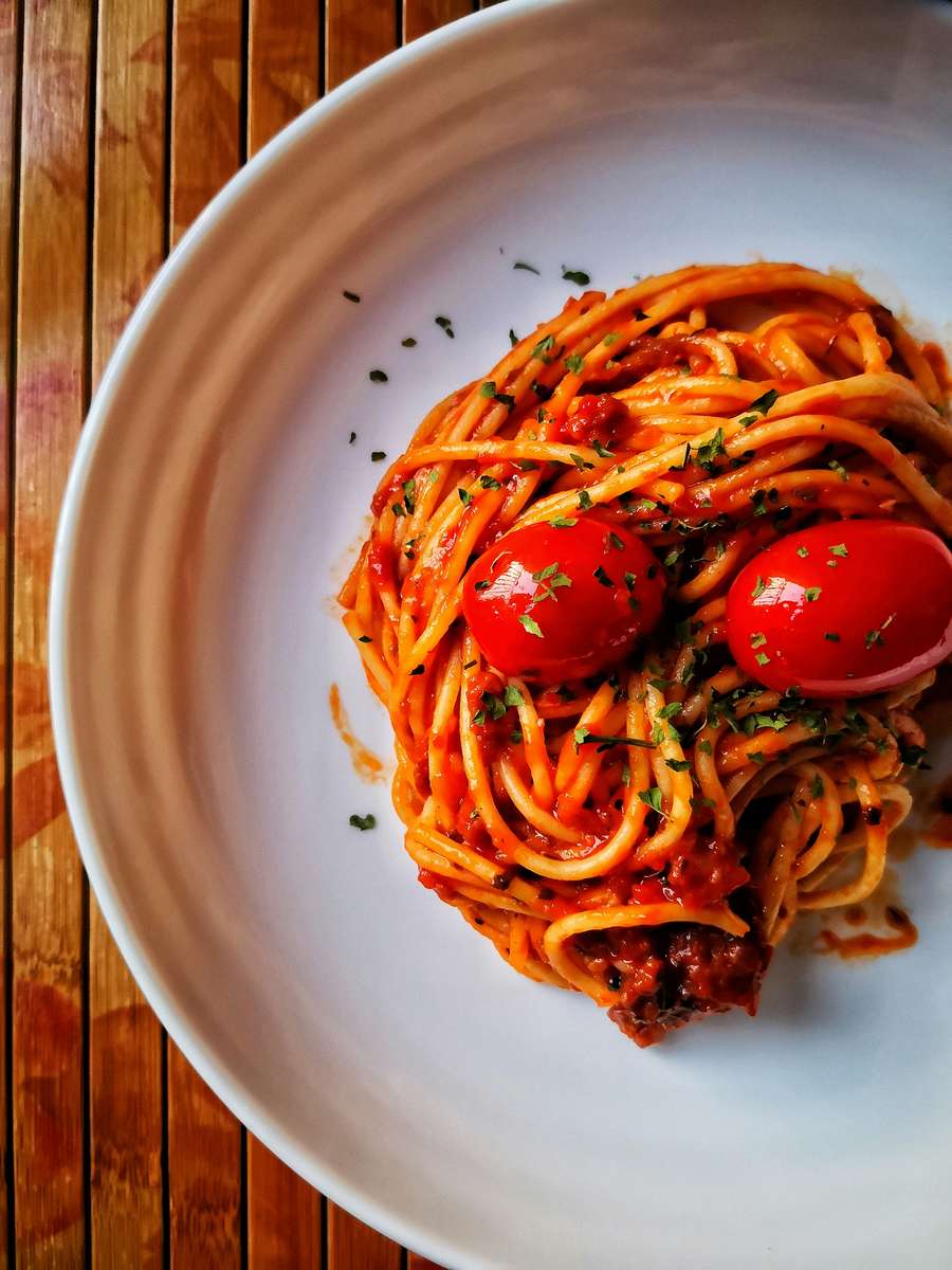 Plate of spaghetti topped with tomato sauce, herbs, and cherry tomatoes