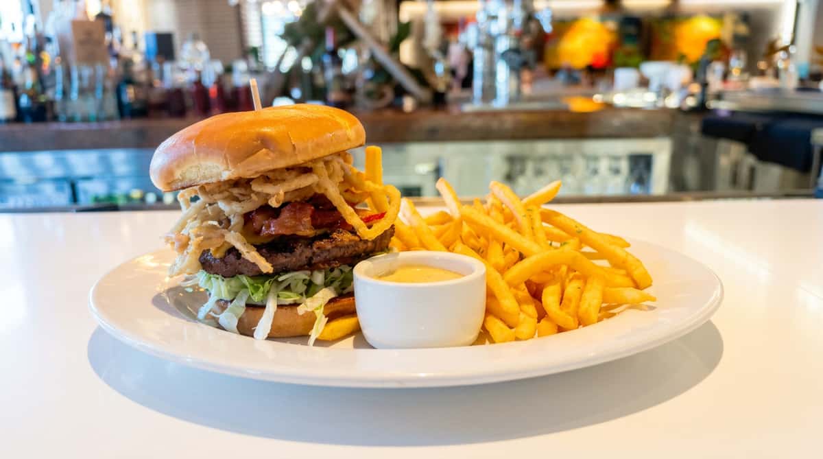 Double patty burger with crispy fried onions, bacon, lettuce, and a side of fries with dipping sauce.