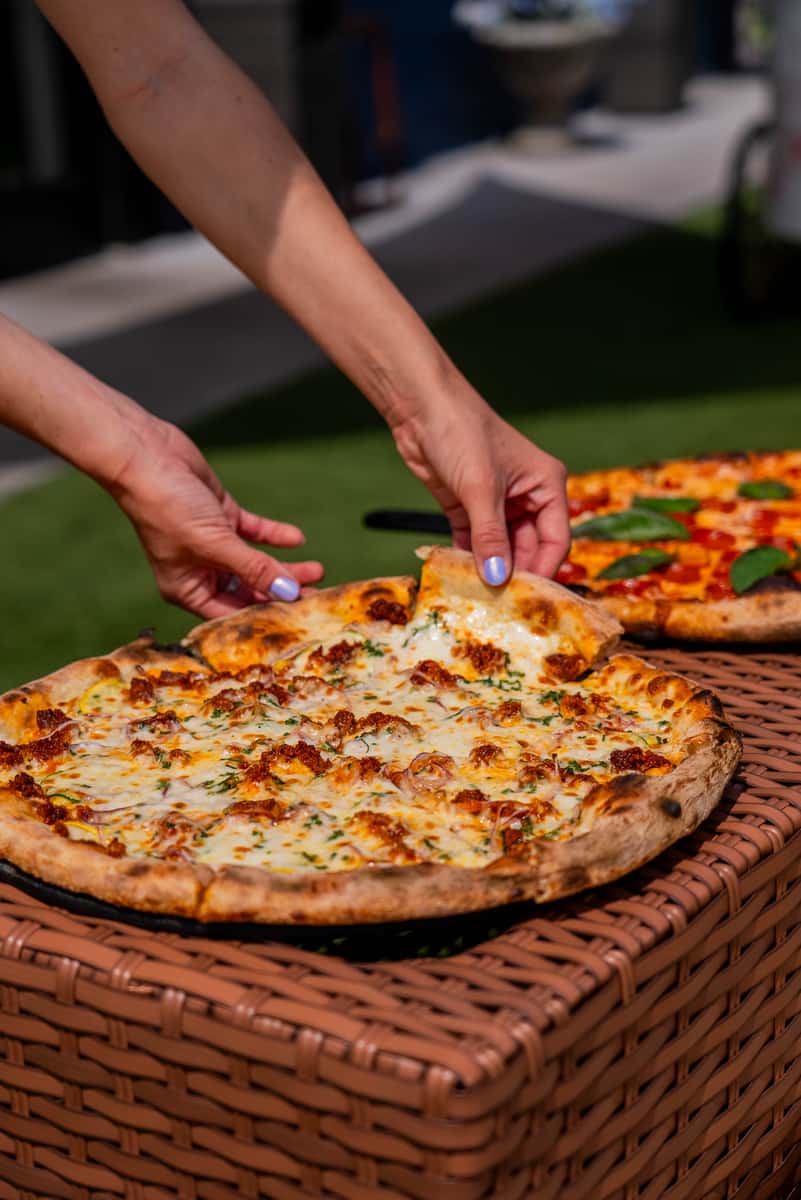 Handcrafted wood-fired pizza with melted cheese and fresh herbs, served on an outdoor patio and perfect for sharing.