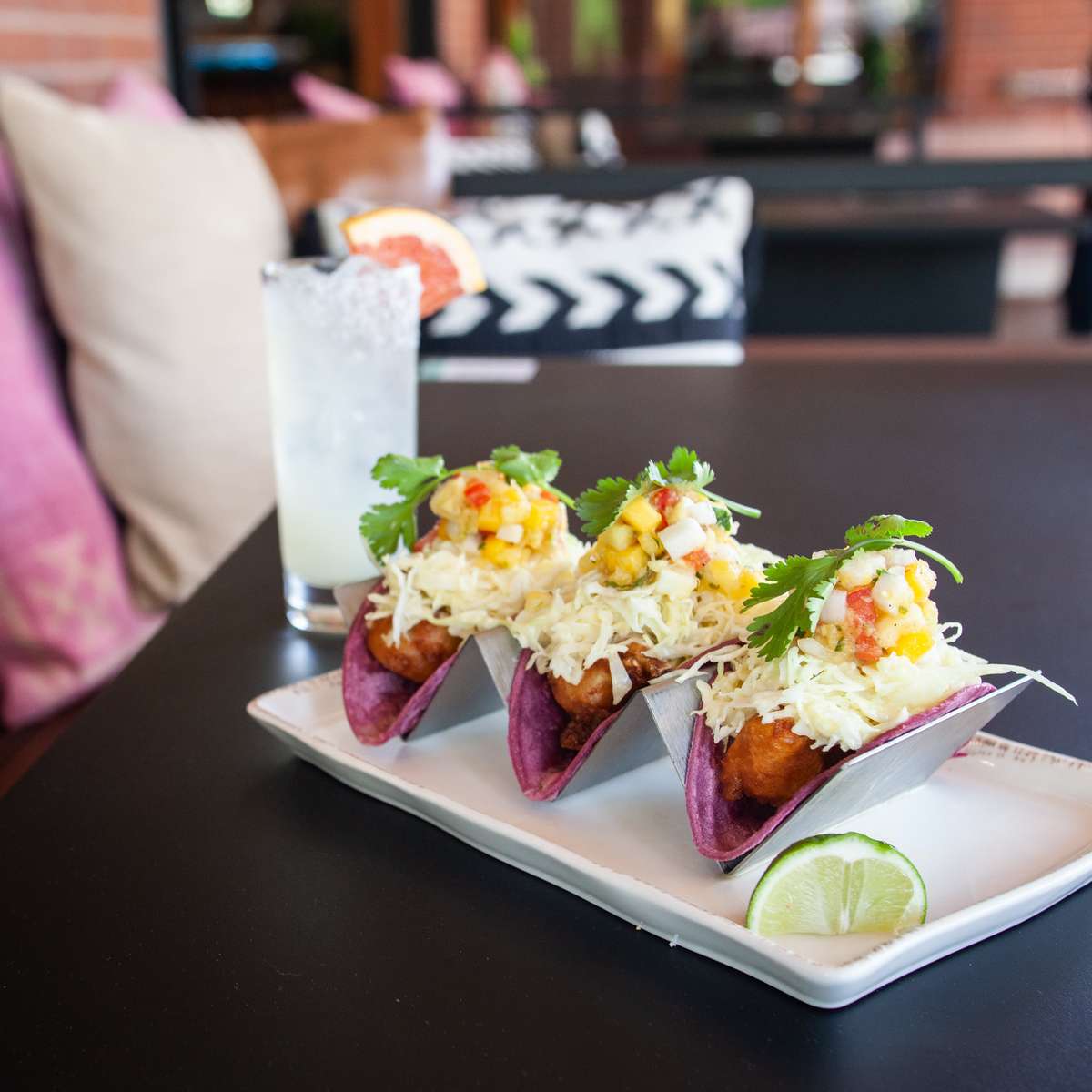 Crispy fish tacos in purple corn tortillas topped with cabbage slaw, fresh pico de gallo, cilantro, and lime, served with a handcrafted cocktail.