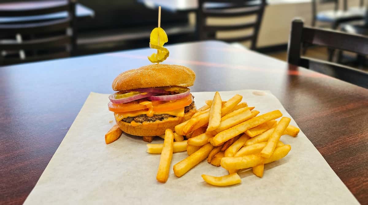 Cheeseburger with melted cheese, tomato, red onion, and pickles, served with golden fries on a paper-lined tray.