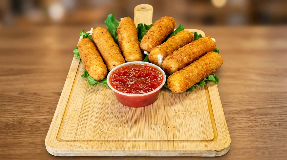 Mozzarella sticks with a side of marinara sauce on a bed of lettuce, served on a light wood cutting board.