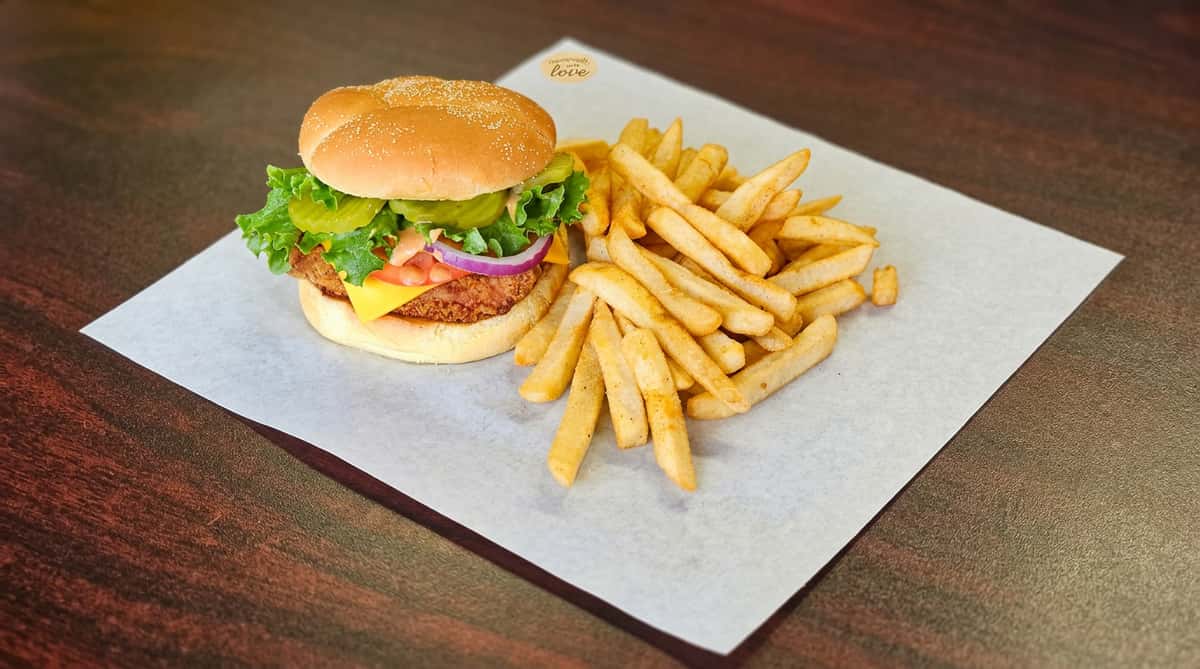 Chicken sandwich with lettuce, pickles, red onion, tomato, cheese, and special sauce, served with golden-brown french fries.
