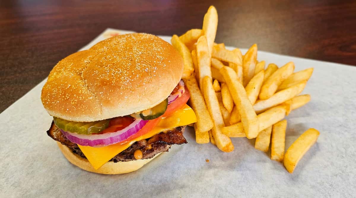 Cheeseburger with lettuce, tomato, onion, pickles, and a side of french fries on parchment paper.