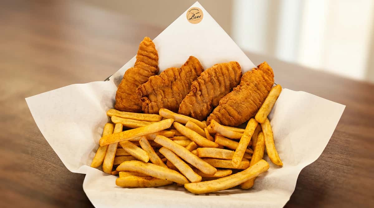 Fried fish fillets and french fries seasoned with spices, served in a black basket lined with white paper.
