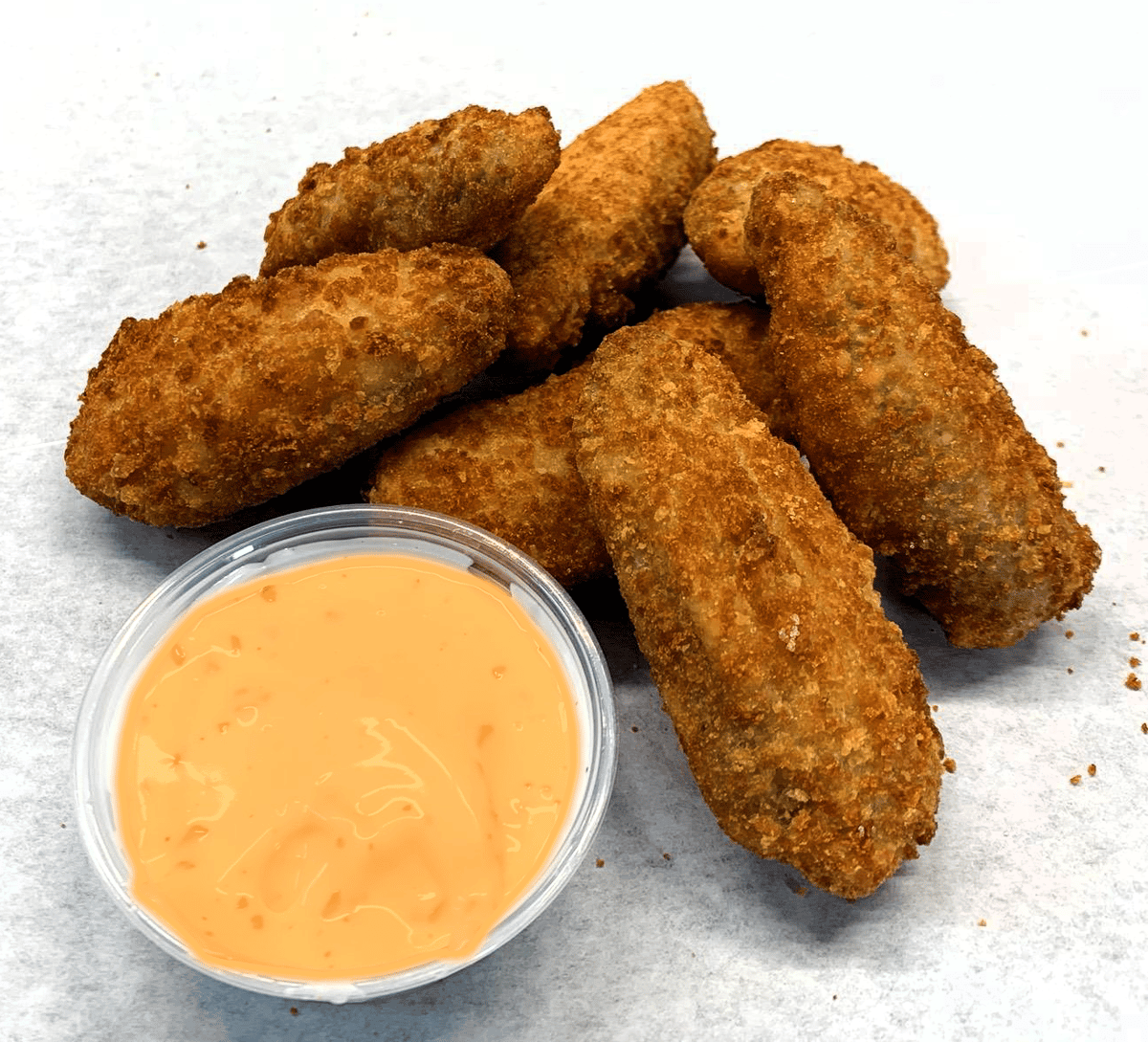 Seven pieces of Jalapeño poppers in a mile next to a cup of dipping sauce