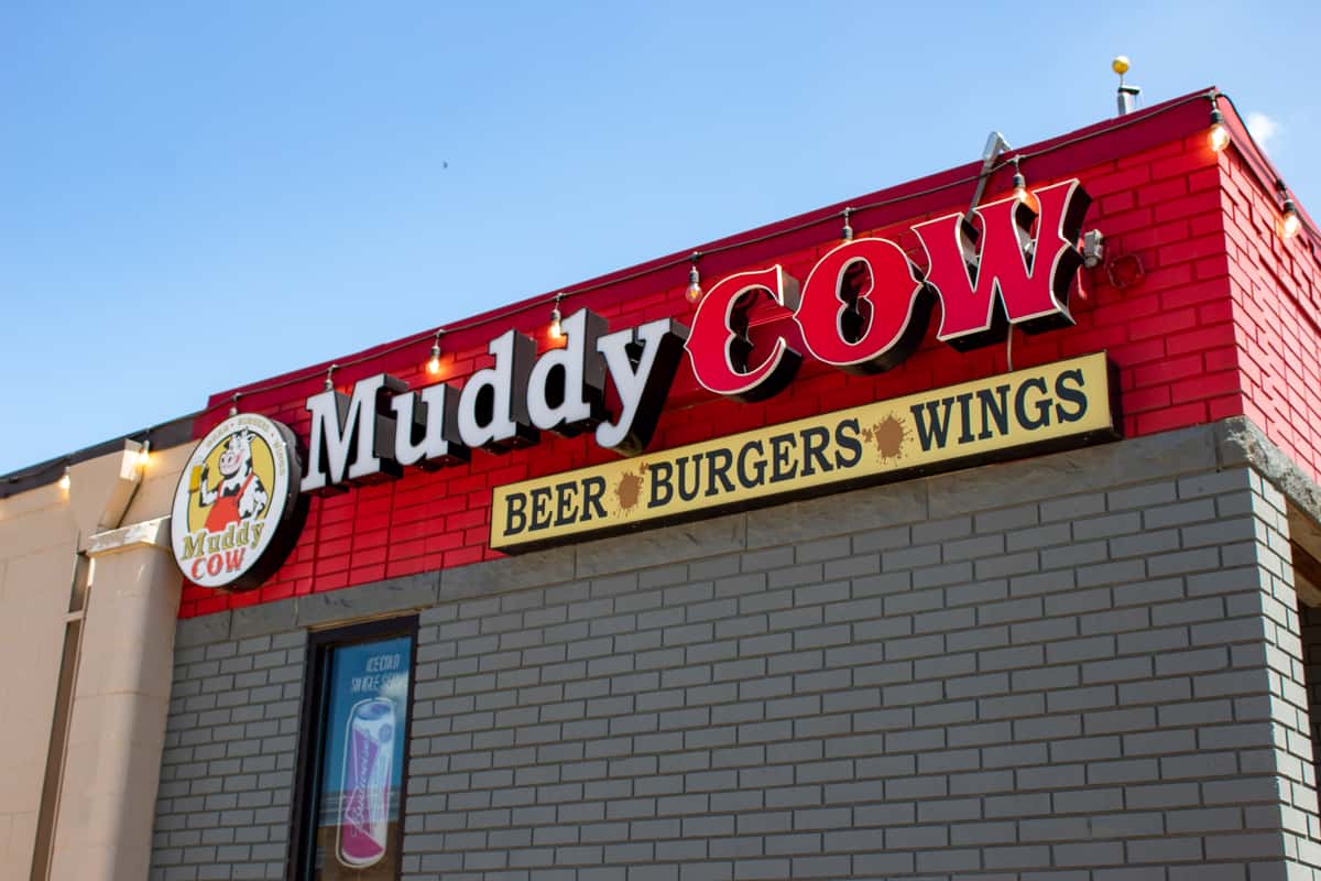 Exterior of the Muddy Cow restaurant. Gray building with lights on top 