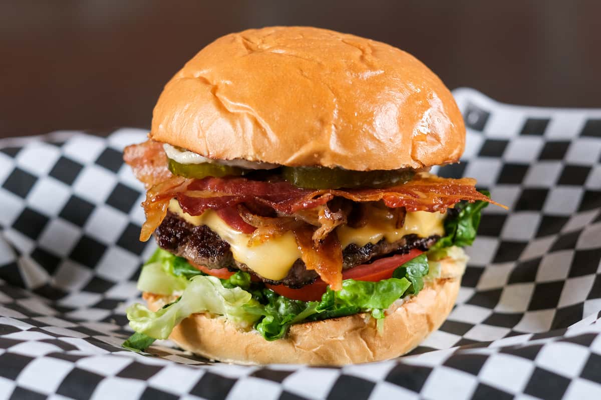 A juicy, fresh-ground beef patty grilled to perfection and topped with melted American cheese and crispy bacon. Stacked with crisp lettuce, ripe tomato, savory grilled onions, and our signature homemade pickles, all served on an artisan bun. Finished with a rich and flavorful garlic mayo for the perfect bite.
