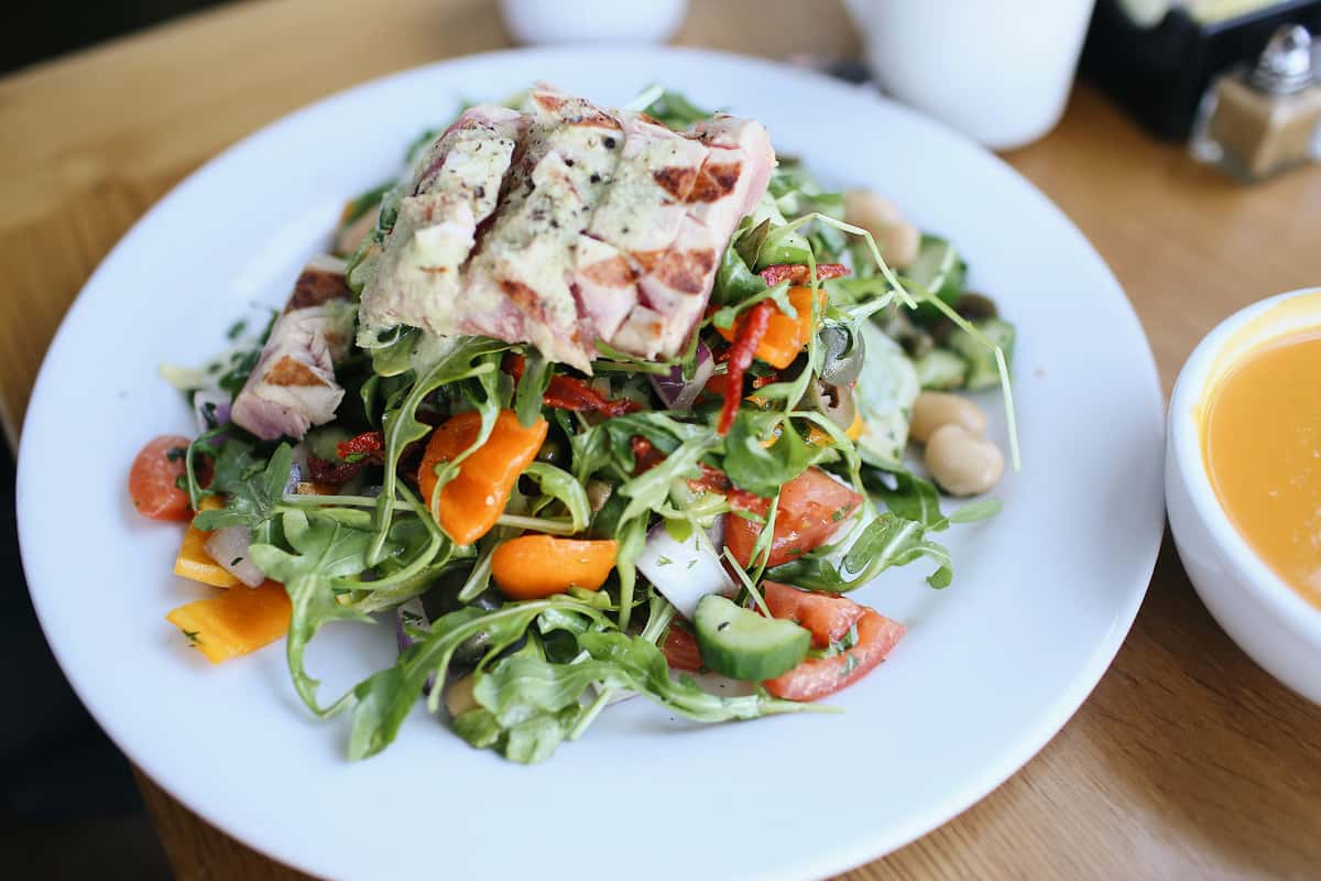 Grilled chicken breast over fresh mixed greens with cherry tomatoes, cucumbers, carrots, red onion, and house dressing—healthy American restaurant salad with vibrant vegetables.
