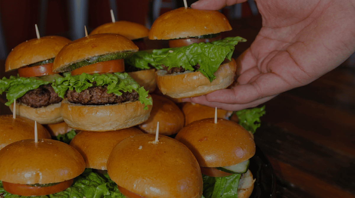 Platter of Social Burger mini sliders with fresh lettuce, tomatoes, pickles, and grilled beef patties, perfect for catering, parties, and group events.