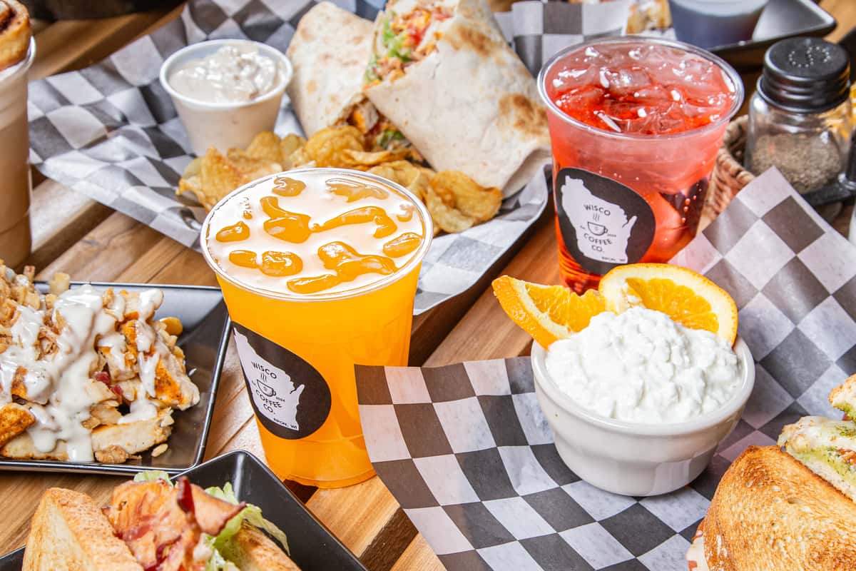 Overhead spread of breakfast waffles, sandwiches, sides, and drinks on rustic wood table
