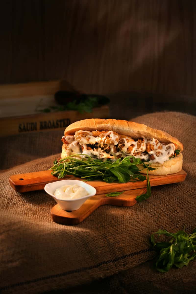 A chicken sandwich with sauce and arugula is served on a wooden board with a side of mayonnaise at Spot Gourmet Burgers.
