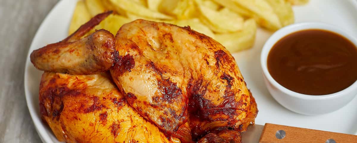 Close-up of grilled chicken quarter with crispy skin and sauce on the side.