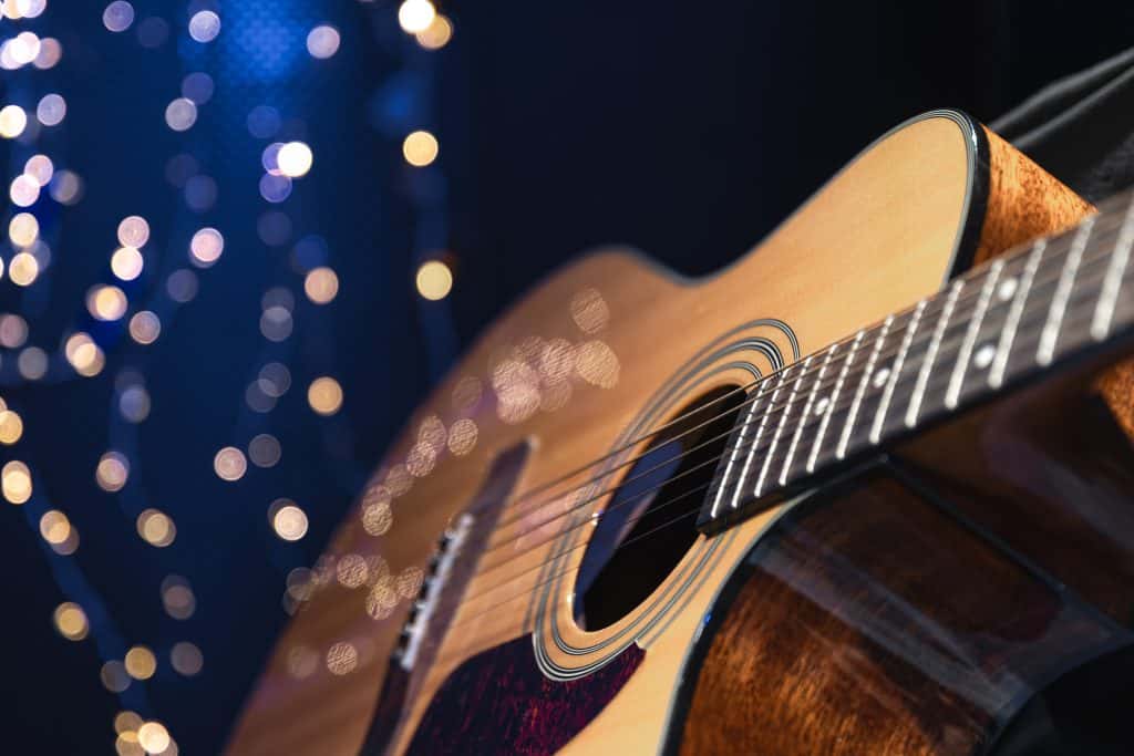 Close-up of an acoustic guitar with a natural wood finish, set against a dark background with warm bokeh string lights, creating a cozy, live music ambiance ideal for restaurant or bar entertainment.