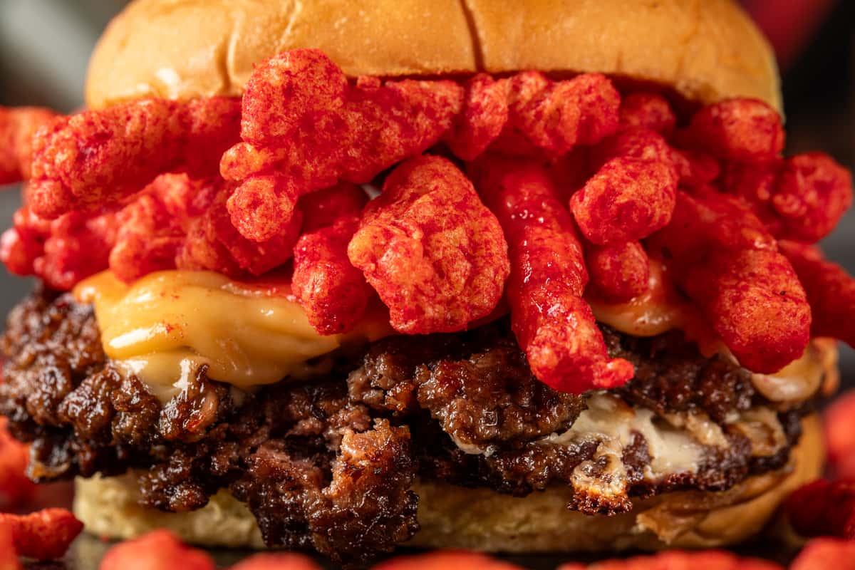 Cheeseburger stacked with spicy Flamin' Hot Cheetos, double beef patties, and melted cheese on a toasted bun.