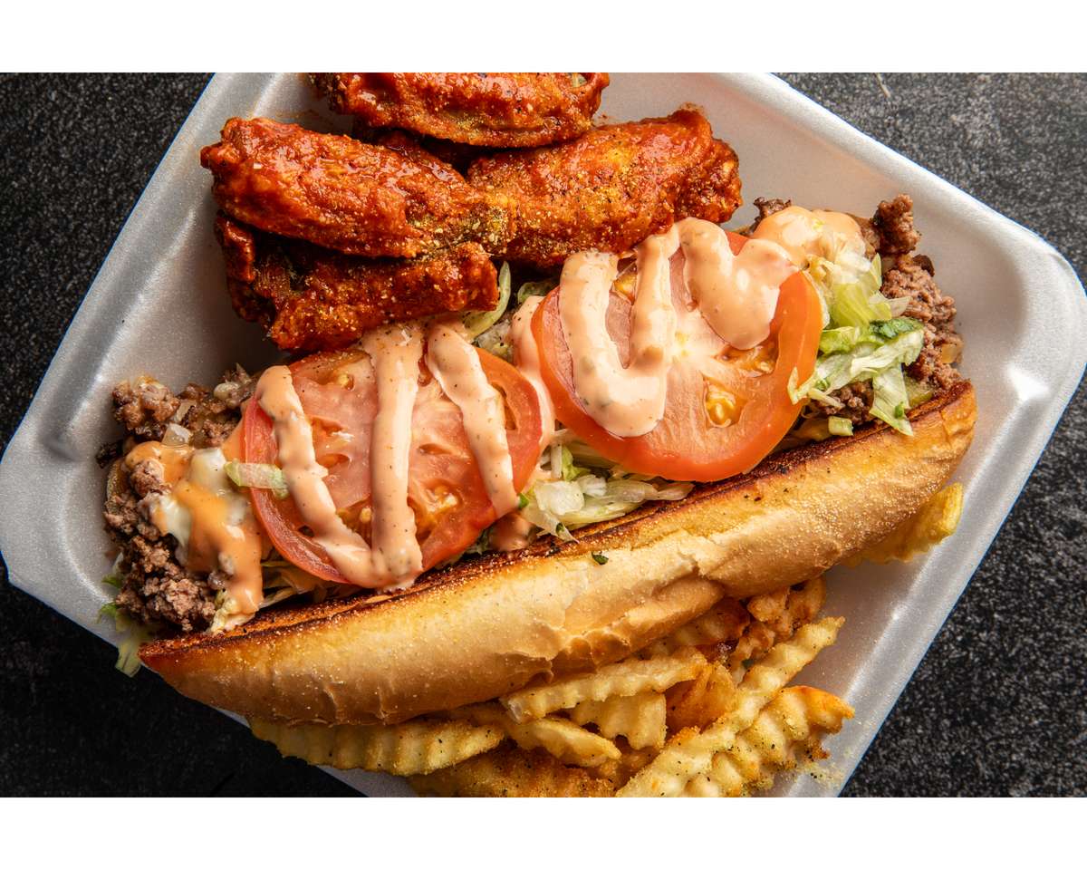 Spicy chicken wings with a cheeseburger sub topped with tomatoes, lettuce, sauce, and a side of seasoned crinkle fries.