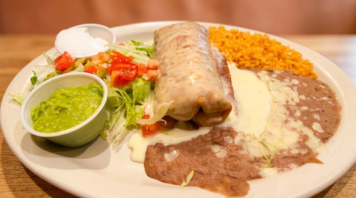 Smothered wet burrito topped with savory sauce and served with Mexican rice, refried beans, and guacamole at Maya Mexican Restaurant.