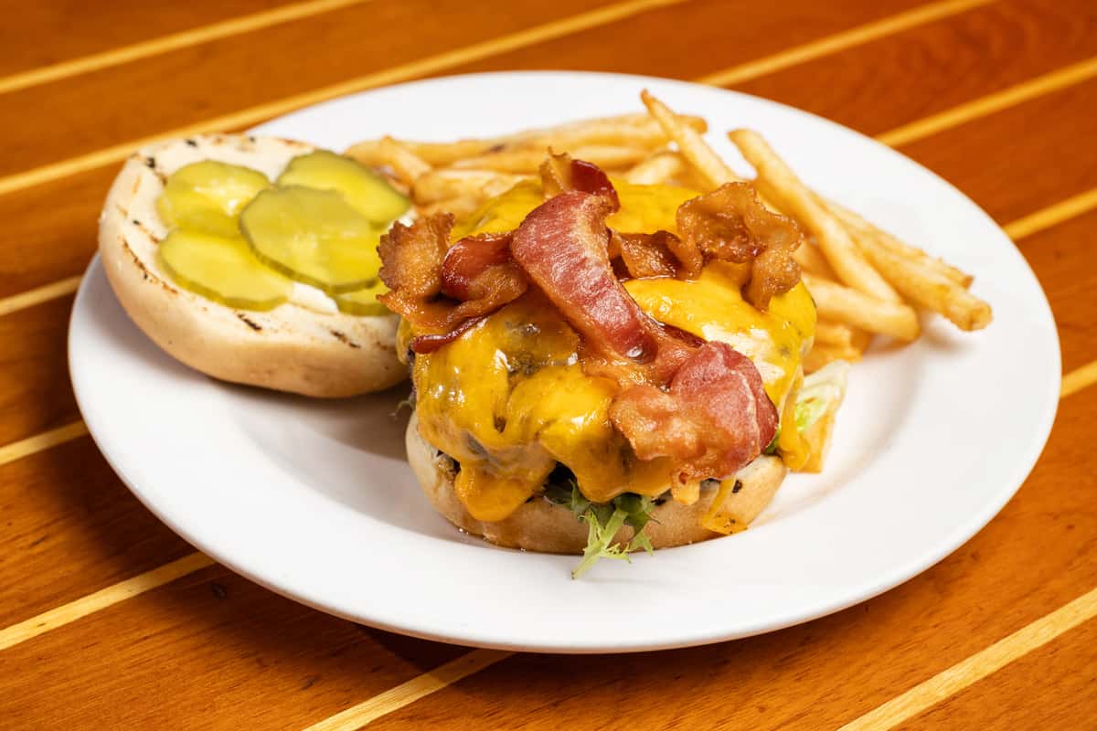 Bacon cheeseburger with a juicy beef patty, melted cheddar cheese, crispy bacon, fresh lettuce, and pickles on a toasted bun, served with French fries at an American bar and grill.