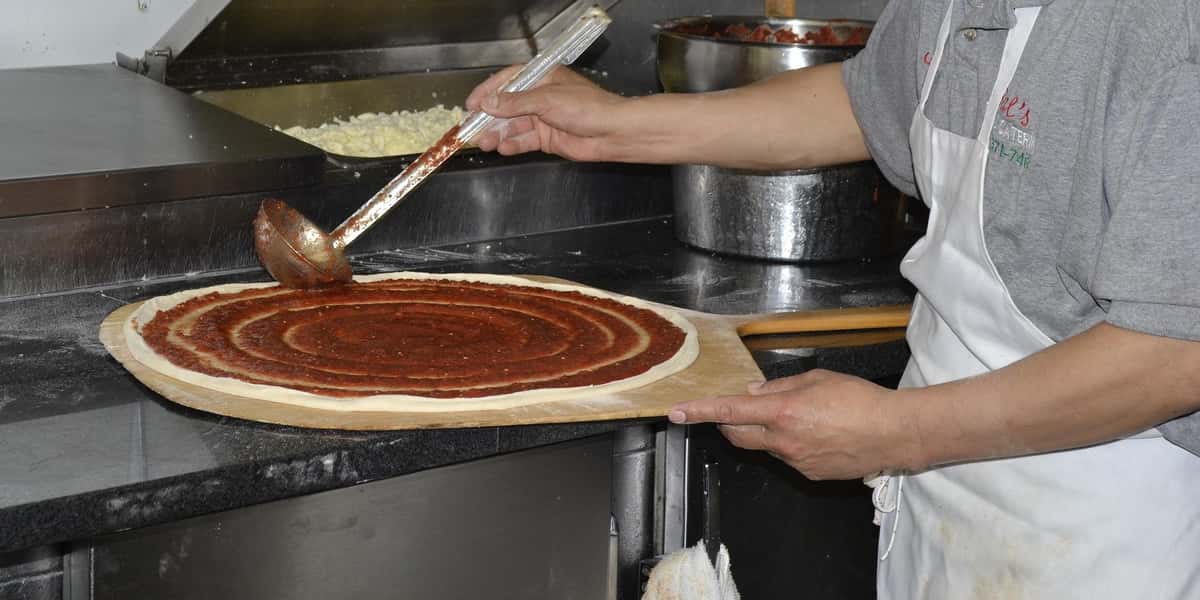 Pizza maker saucing a pizza base