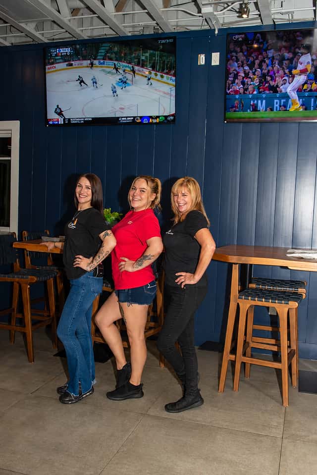 Fin & Tonic team smiling beside the navy walls and warm wood seating in Sarasota — approved edited professional portrait