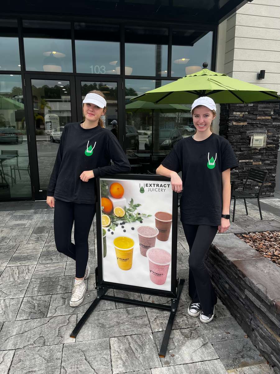 Two people standing in front of an Extract Juicery sign