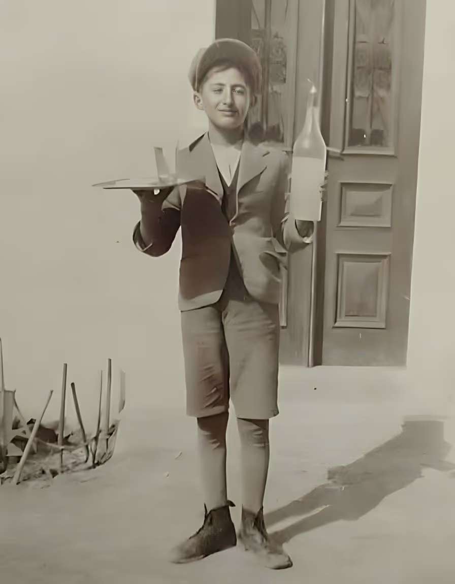 Historic photograph of Cafeneo founder's father as a young boy carrying a serving tray and bottle, celebrating generations of Greek hospitality behind the family-owned café in Newark, Delaware.