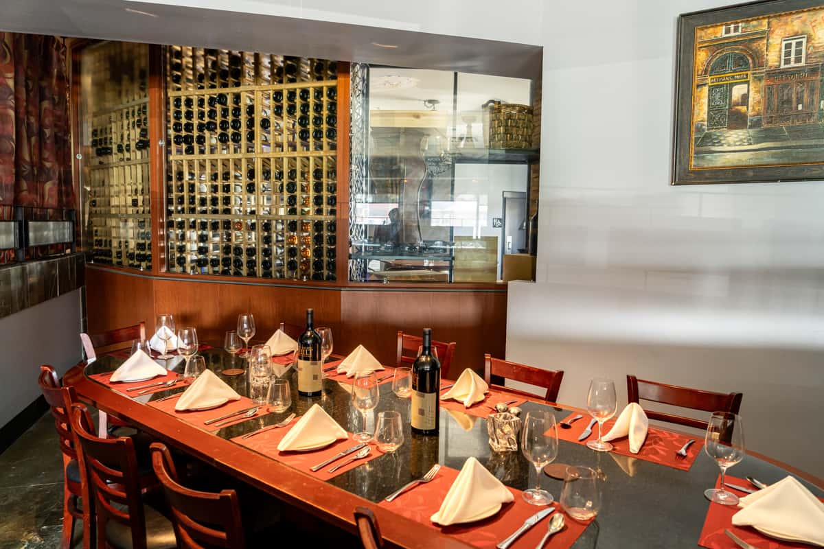 Inside 17th Street Grill, a refined private event space in Tustin, CA, featuring a wine wall display, elegant red dining chairs, and set tables with red napkins, ready to host an intimate gathering