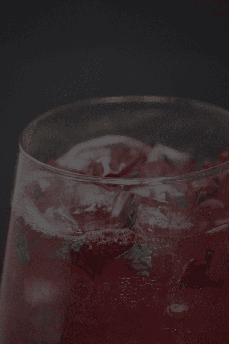 amber cocktail with ice and garnish on a bar counter with greenery