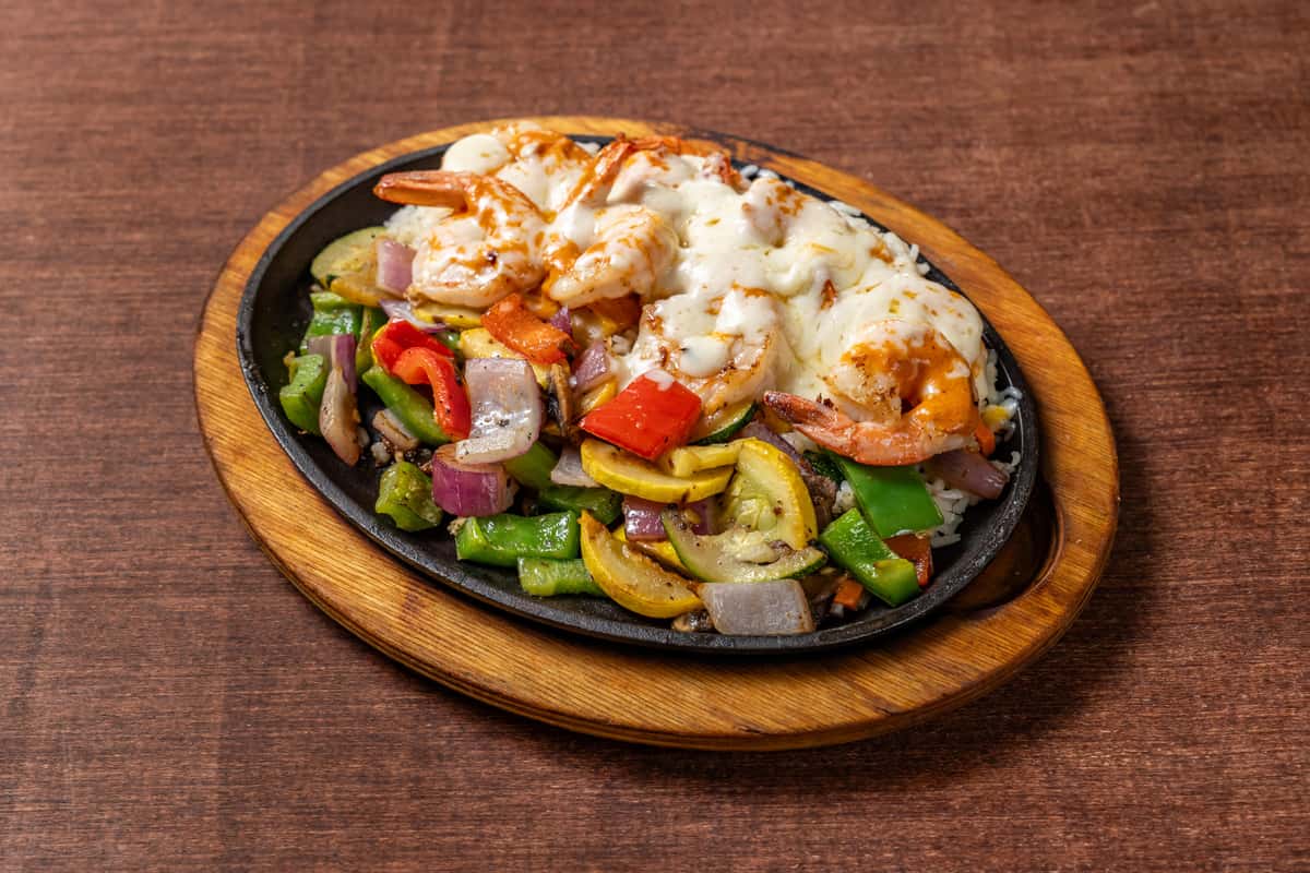 Shrimp fajitas with grilled vegetables and melted cheese over rice, served on a hot skillet with colorful bell peppers and onions.