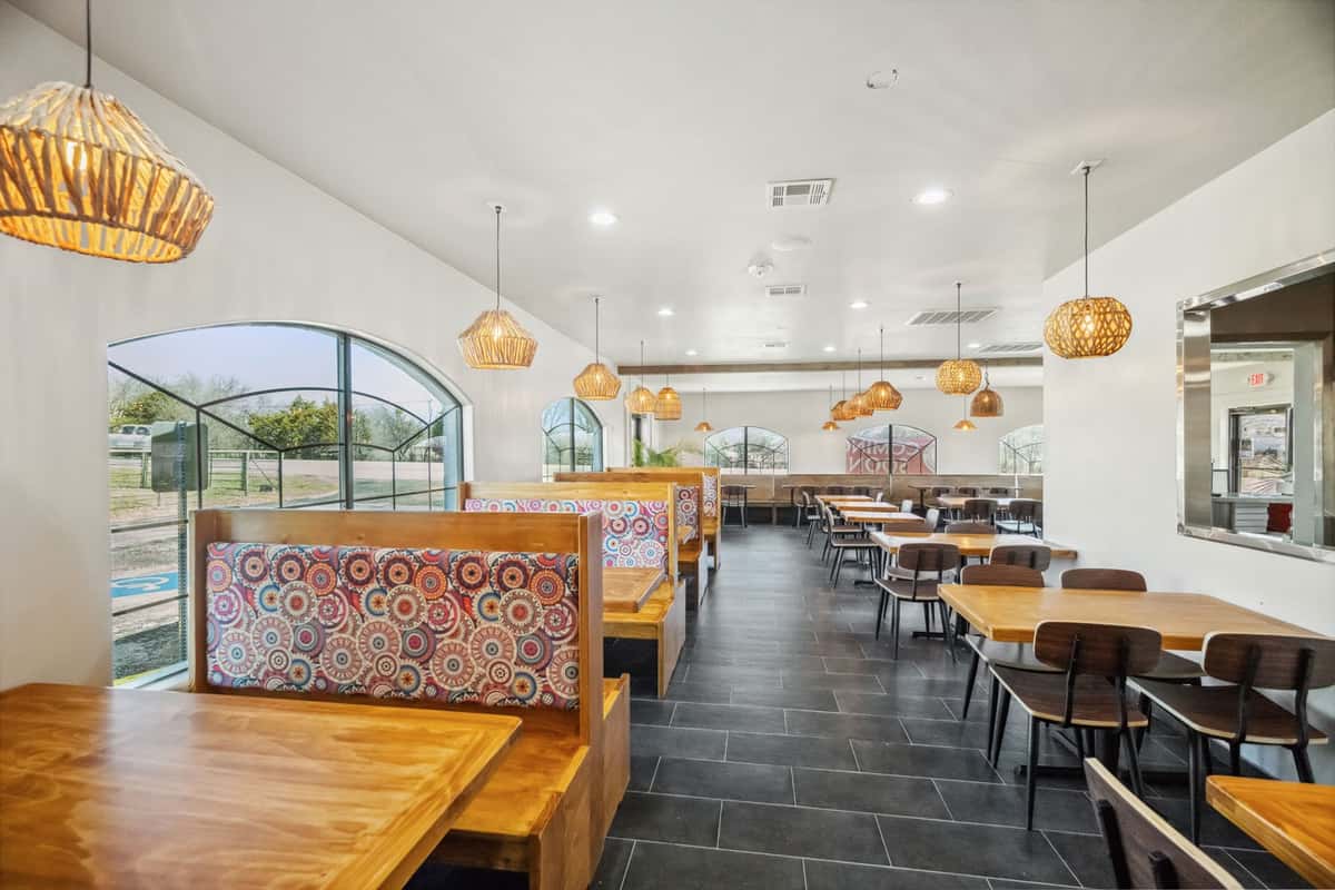 Bright and modern restaurant interior with wooden booths featuring colorful patterned backs, pendant lighting, and black tiled flooring.