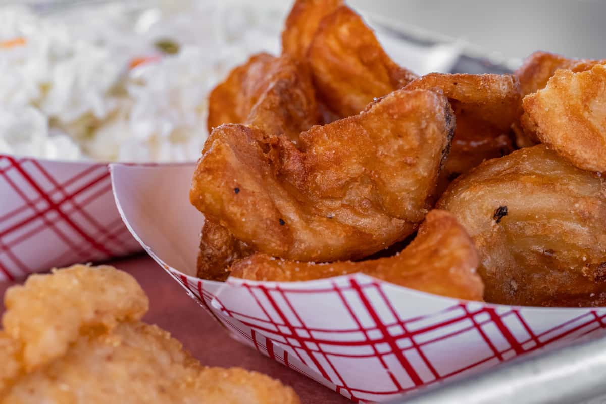 Crispy seasoned potato wedges served in a red-and-white paper tray, accompanied by creamy coleslaw and a portion of breaded fried chicken — classic American comfort food ideal for casual dining or fast food menus.