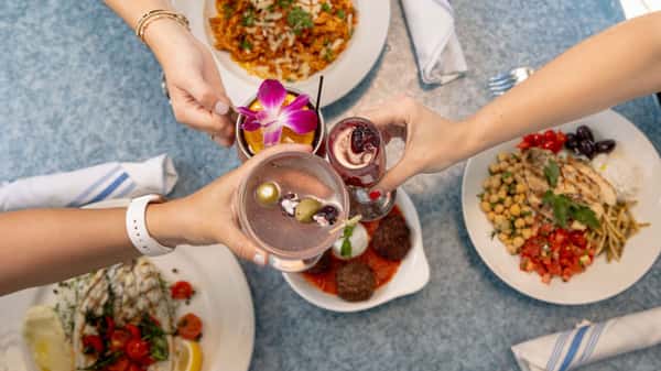 Group of Diners cheering with cocktails and greek food on table