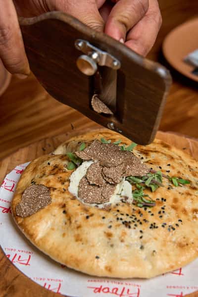 A chef delicately shaves black truffles over a warm, freshly baked naan topped with herb-infused butter, showcasing a luxurious twist on traditional Indian cuisine.