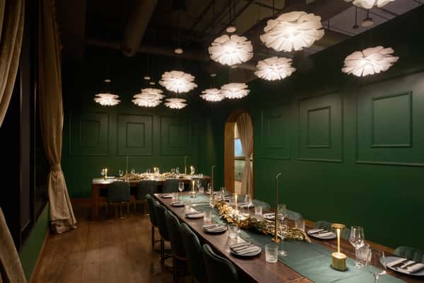 An elegant private event space in Santa Monica, featuring a long wooden table set with fine dining ware, surrounded by plush seating and illuminated by stylish floral pendant lights.