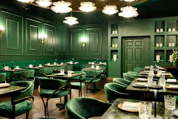 A stylish private event space featuring emerald green walls, plush seating, and elegant tables set with glassware, creating an intimate atmosphere for gatherings and celebrations.