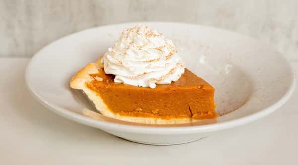 Slice of pumpkin pie topped with a generous swirl of whipped cream on a white dessert plate.