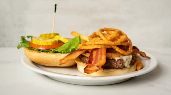 Juicy bacon cheeseburger topped with crispy onion rings, lettuce, tomato, and melted cheese, served with a pickle and golden French fries.