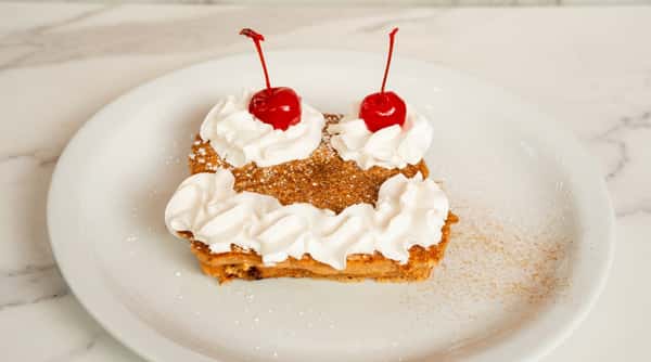 Golden French toast topped with whipped cream, sweet crumble, and two red maraschino cherries.