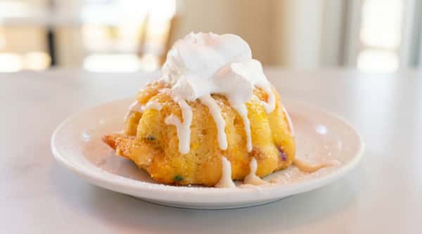 Golden dessert topped with sweet glaze and a generous swirl of whipped cream, served on a white plate.